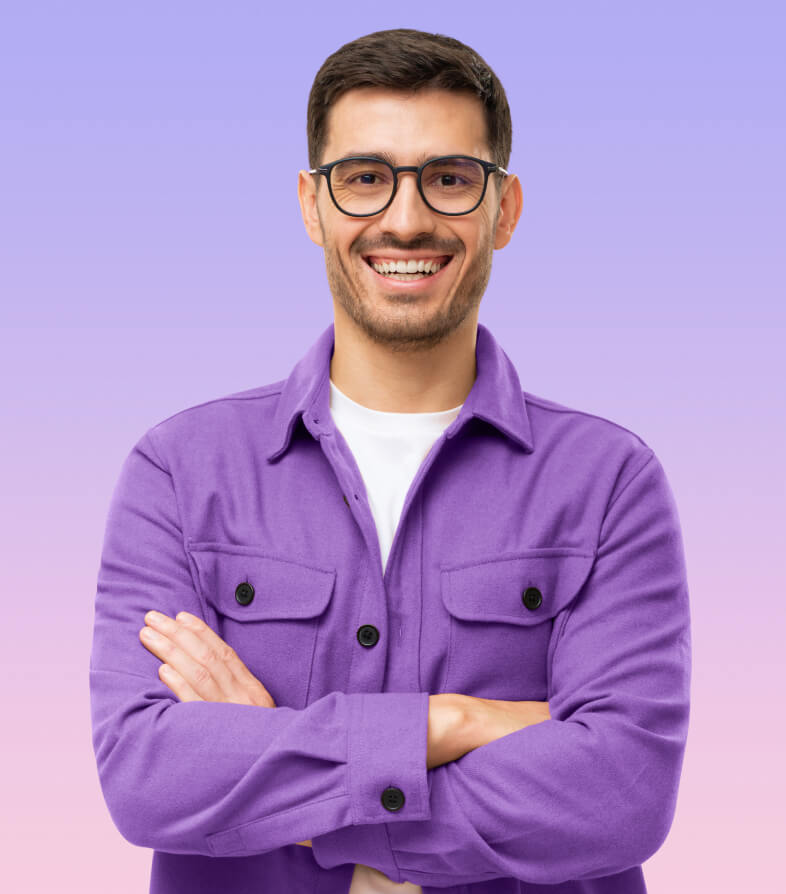 Friendly young man in a purple button up shirt and glasses smiles while looking directly at the camera with his arms crossed