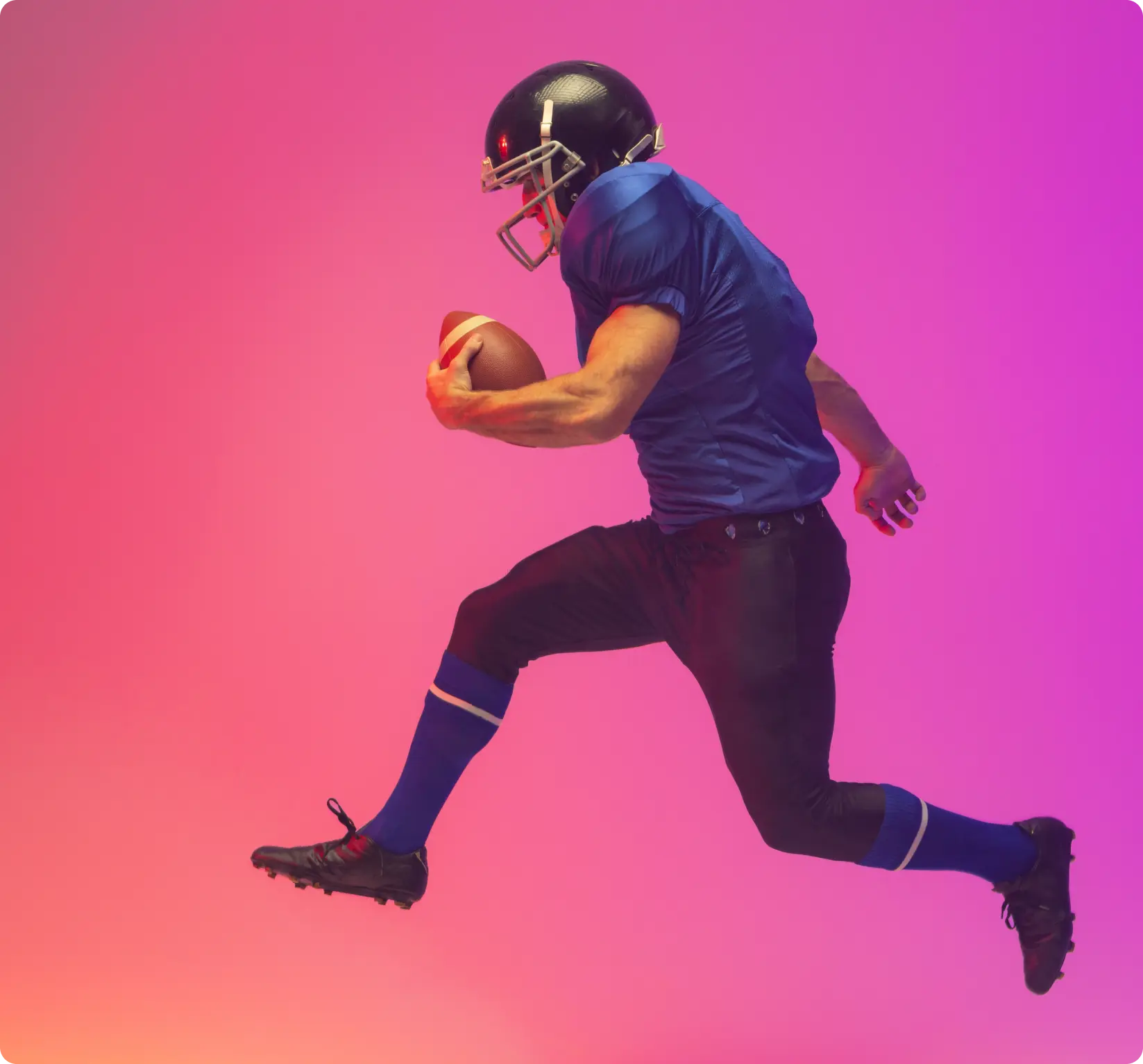 Soccer/Football athlete wearing a blue shirt and black football helmet jumping while holding a football in his hand