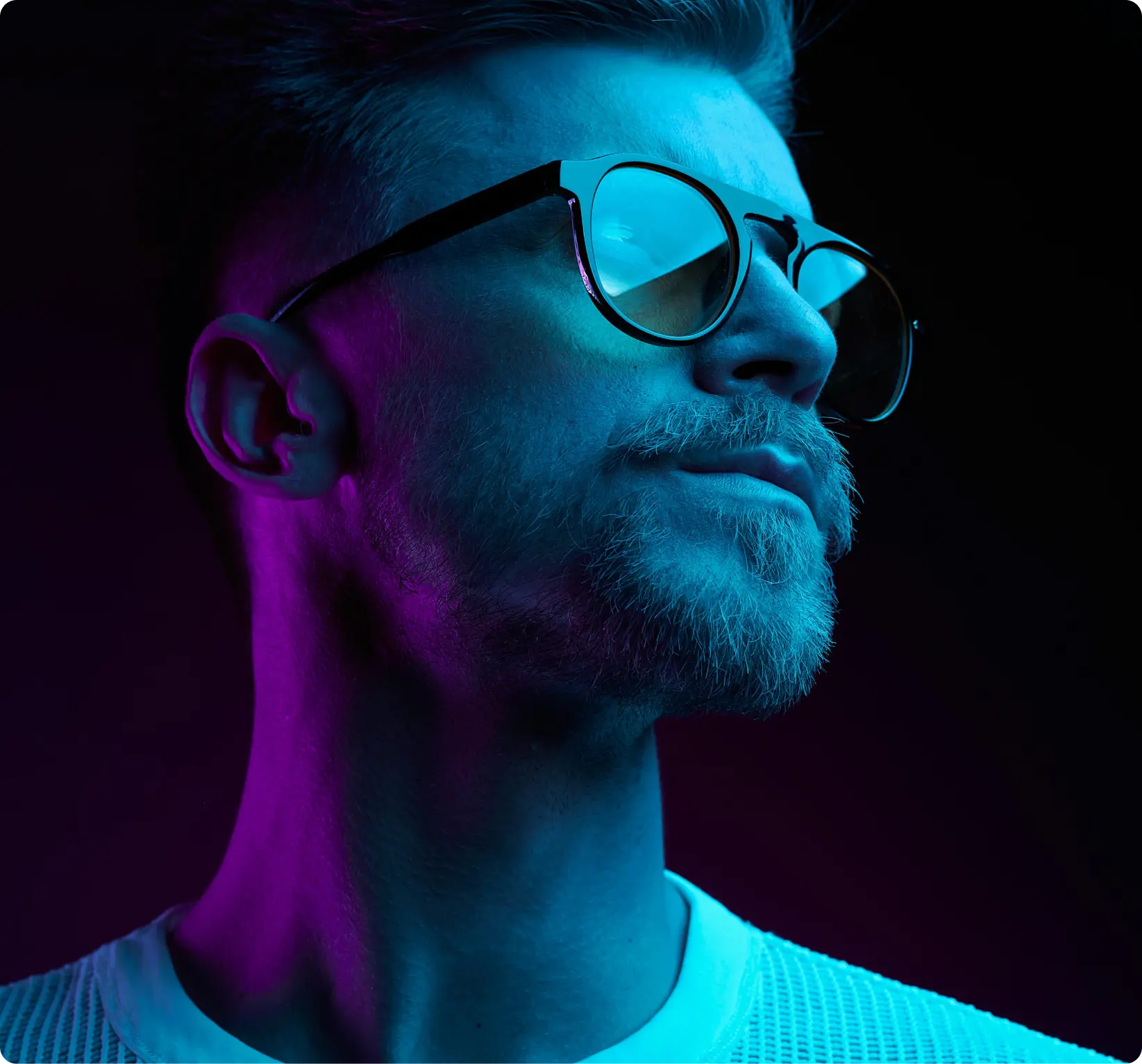 Young man with sunglasses looks to the distance with blue and pink neon lights on him